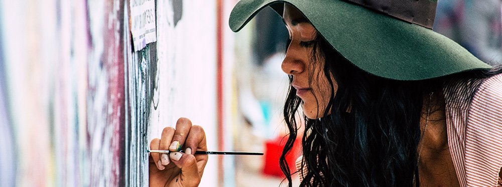 A woman paints a colorful wall with a fine paint brush