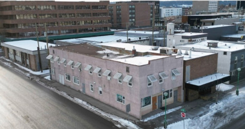 Low-rise grey building on a street corner in Prince George, shown on a rainy day.