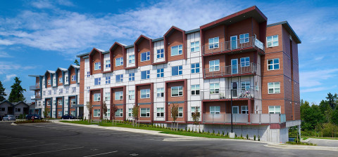 White and brown sided four storey apartment building built on a slanted parking lot