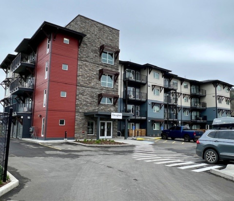 Corner view of a four-storey building with partial brickwork and white and blue siding.