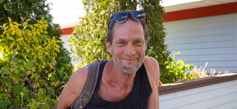 Middle-aged man wearing a backpack, smiling, with sunglasses resting on top of his head.