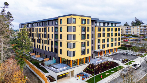 A modern six-storey apartment building with yellow siding and street-level landscaping in an urban residential neighbourhood.