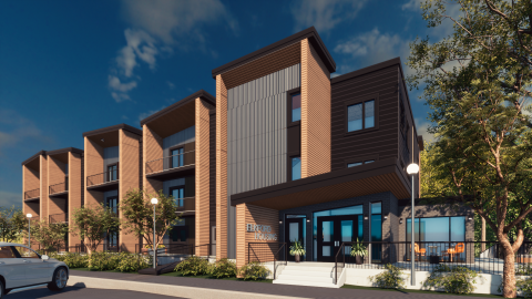 Modern multi-story apartment building with wooden and dark-colored panels, large windows, and balconies, surrounded by landscaped greenery.