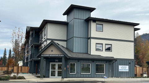 Three-story building with gray siding and a grand opening sign, featuring large windows