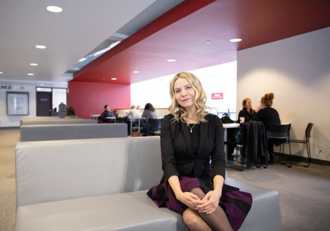 A blond woman sits on a grey couch