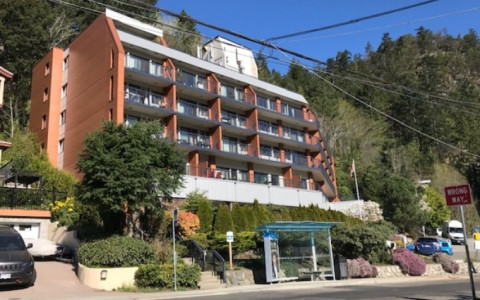 Front view of a low rise brown and white building on a hill. Green bushes and trees surround the building