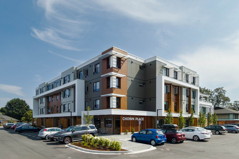 Angled view of a four-storey building with cars parked in spaces surrounding the structure.