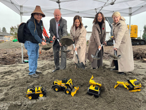 Five representatives shovelling site dirt, with five yellow Tonka trucks displayed in front of them.