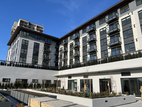 Modern mid-rise apartment building with balconies and a landscaped courtyard under a clear blue sky.