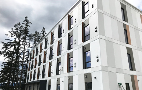 Exterior of Sq'umul' Shelh Lelum', a modern four-storey building with white and grey panels located at 6428 Paddle Road.