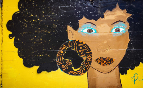 Mural of a black woman with short curly hair wearing black and orange circular earrings on yellow background