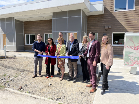 A group of people gathered to cut a large blue ribbon, marking the opening of twenty-five new affordable homes.