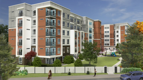 A modern five-storey apartment complex with red brick and white paneling, featuring balconies and large windows. The landscaped courtyard includes green lawns, trees, and a small playground, with a white fence and sidewalk in the foreground.