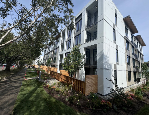 Modern apartment building with balconies, surrounded by greenery and a clear sky.
