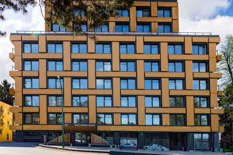 Exterior of a mid-rise with tan panels and blue windows, framed by trees; entrance labeled Chief Leonard George.