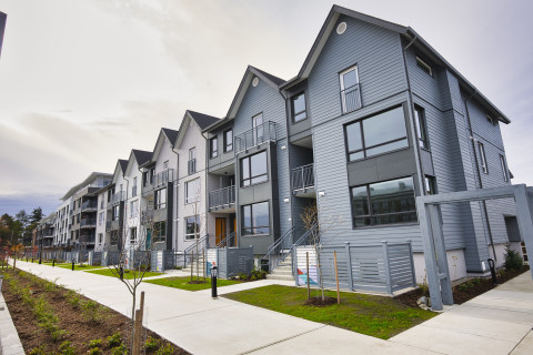 Modern grey townhouse and apartment complex with balconies, landscaped walkways, and shared green spaces.