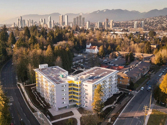 An aerial view of a residential area featuring a modern, multi-story apartment building with white and yellow accents.