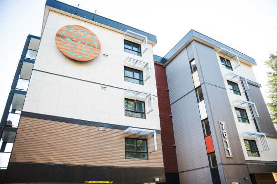 Five-storey apartment building with a circular Indigenous art piece displayed on its exterior wall.