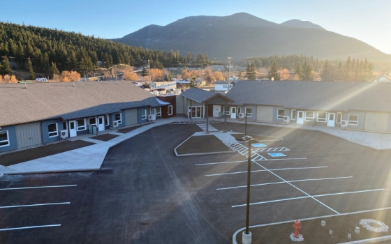 Two rows of single-storey housing with a mountain in the background and a parking lot in the foreground.