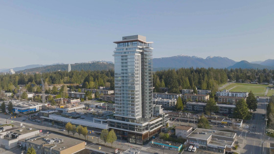 Aerial view of a 25-storey apartment tower standing tall above neighbouring stores and housing units.