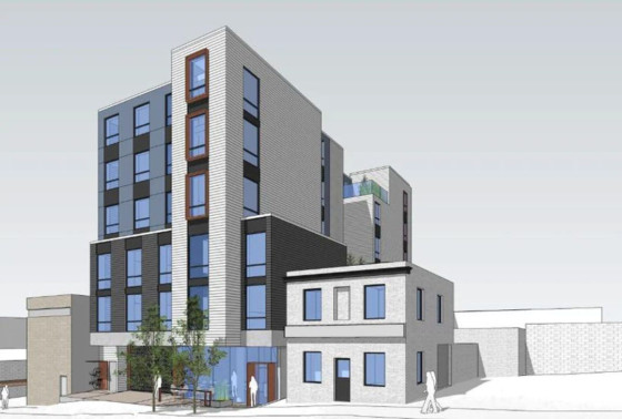 Rendering of a modern multi-storey building with grey and white exterior walls, large windows, and wooden accents. The structure includes a taller section and a shorter, more traditional section on the right, with trees and greenery near the entrance and a few people walking nearby.