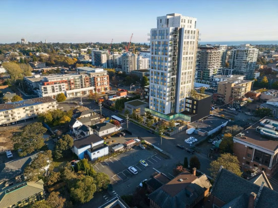 Aerial view of an urban neighbourhood in Victoria, BC, with a rendering of a 21-storey residential high-rise prominently standing among low-rise buildings, townhouses, and other apartment complexes.