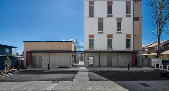 A modern multi‑storey building with a gated entrance and ground‑level walkway on a sunny day.
