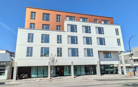 Modern five-storey mixed-use building with white and terracotta exterior, large windows, and street-level commercial space.