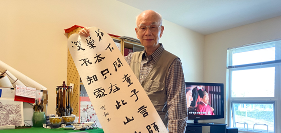 Mr Mak, elderly smiling Asian man proudly holds his wife's caligraphy
