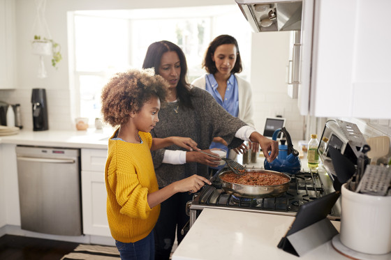 Three generations of a family cooking together in a bright kitchen, symbolizing home stability and togetherness.
