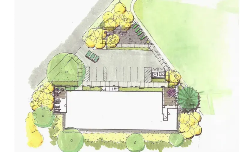 A coloured site plan showing a rectangular building centered at the bottom of the layout, surrounded by landscaped areas with trees. A parking lot with multiple marked stalls sits above the building, along with pathways, planted areas, and small seating zones. A curved path runs along the top right of the site.