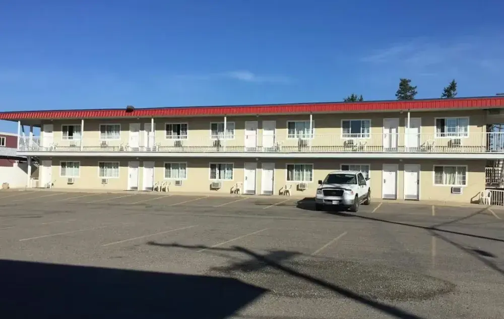 Two‑storey motel‑style building with a red roof, seen from a parking lot on a clear day.