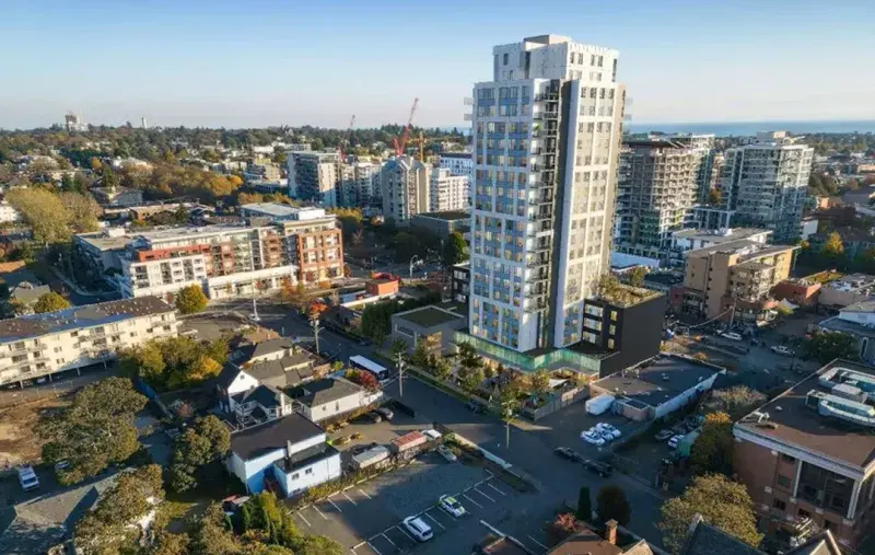 Aerial view of a tall residential tower surrounded by city streets, low-rise buildings, and distant ocean horizon.